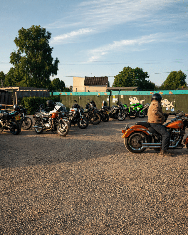 Row of motorcycles parked at Buckovers Bike Night with a rider arriving across the car park.